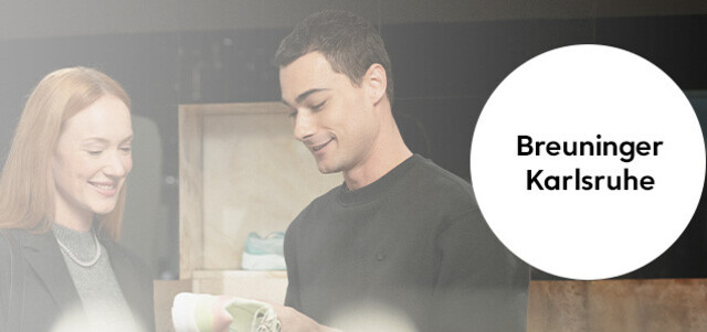 Zwei Personen stehen im Gespräch in einem Modegeschäft; rechts ein runder Hinweis mit der Aufschrift „Breuninger Karlsruhe“, Verkaufsfläche und Kund:innen unscharf im Hintergrund.